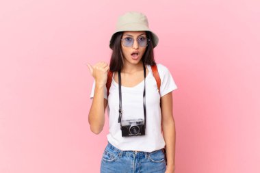 pretty hispanic tourist looking astonished in disbelief with a photo camera and a hat