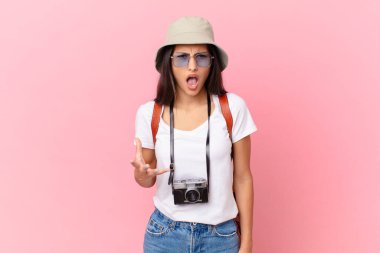 pretty hispanic tourist looking angry, annoyed and frustrated with a photo camera and a hat