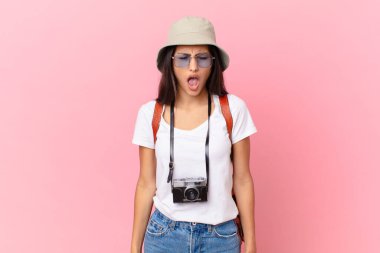 pretty hispanic tourist shouting aggressively, looking very angry with a photo camera and a hat