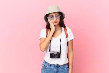 pretty hispanic tourist feeling bored, frustrated and sleepy after a tiresome with a photo camera and a hat