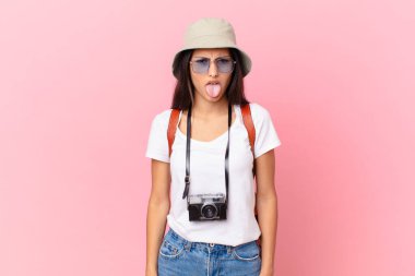 pretty hispanic tourist feeling disgusted and irritated and tongue out with a photo camera and a hat