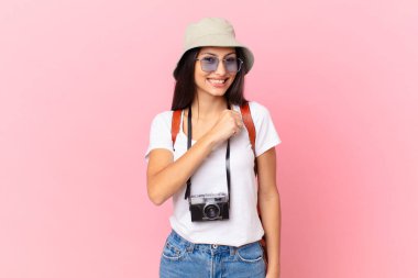 pretty hispanic tourist feeling happy and facing a challenge or celebrating with a photo camera and a hat