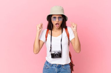 pretty hispanic tourist shouting aggressively with an angry expression with a photo camera and a hat