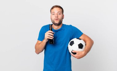 Elinde bira ve futbol topu olan yakışıklı bir adam.
