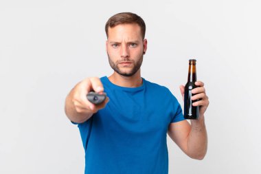 Yakışıklı adam elinde birayla televizyon seyrediyor.