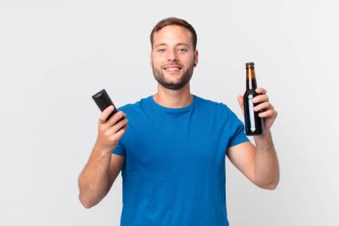 Yakışıklı adam elinde birayla televizyon seyrediyor.