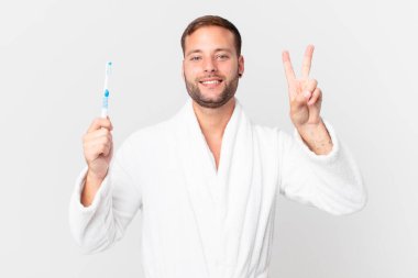 Bornoz giyen ve elinde diş fırçası tutan yakışıklı bir adam.