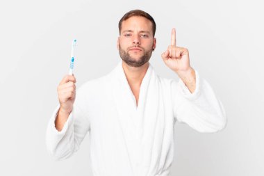 Bornoz giyen ve elinde diş fırçası tutan yakışıklı bir adam.