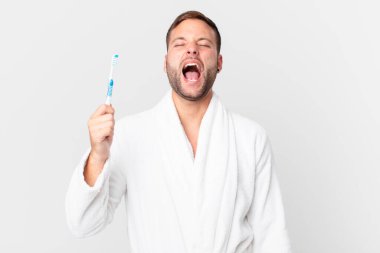 Bornoz giyen ve elinde diş fırçası tutan yakışıklı bir adam.