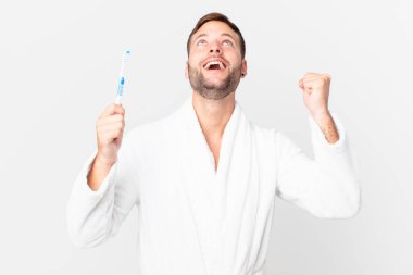 Bornoz giyen ve elinde diş fırçası tutan yakışıklı bir adam.