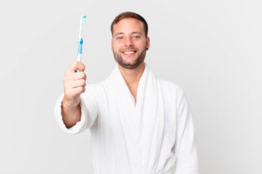 Bornoz giyen ve elinde diş fırçası tutan yakışıklı bir adam.