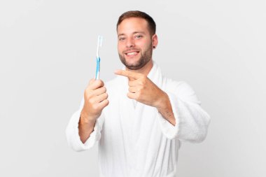 Bornoz giyen ve elinde diş fırçası tutan yakışıklı bir adam.