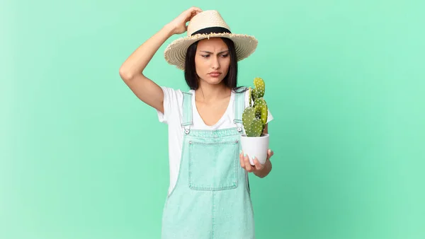 Pretty Farmer Woman Feeling Puzzled Confused Scratching Head Holding Cactus — Stockfoto