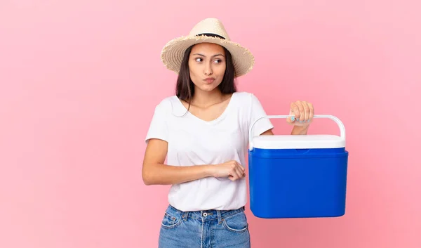 Pretty Hispanic Woman Shrugging Feeling Confused Uncertain Holding Portable Refrigerator — Stockfoto