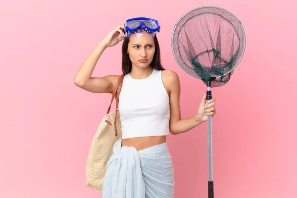 young fisher woman feeling puzzled and confused, scratching head and and diving goggles