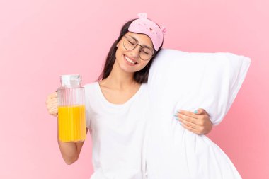 hispanic pretty woman wearing pajamas and holding a pillow and an orange juice