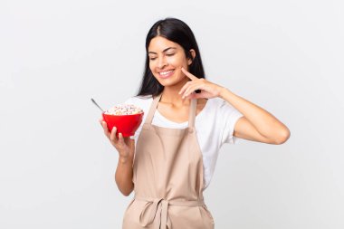 Güzel İspanyol kadın güzel İspanyol şef kadın mutlu bir şekilde gülümsüyor ve hayal kuruyor ya da şüphe ediyor ve elinde mısır gevreği kasesi tutuyor.