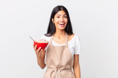 Güzel İspanyol kadın güzel İspanyol şef kadın mutlu ve hoş bir şekilde şaşırmış ve elinde mısır gevreği kasesi tutuyor.