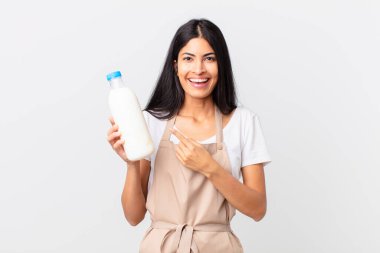 Güzel İspanyol aşçı kadın heyecanlı ve şaşırmış görünüyor. Yan tarafı gösterip elinde süt şişesi tutuyor.