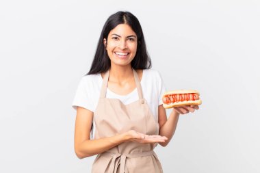 İspanyol güzel kadın güzel İspanyol şef kadın neşeyle gülümsüyor, mutlu ve bir konsept gösteriyor ve bir sosisli sandviç tutuyor.