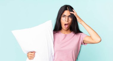 Güzel İspanyol kadın mutlu, şaşkın ve şaşırmış görünüyor ve yastıklı pijama giyiyor.