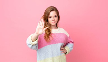 Güzel kızıl saçlı kadın ciddi görünüyor. Avuç içini gösteriyor. Durdurma hareketi yapıyor.