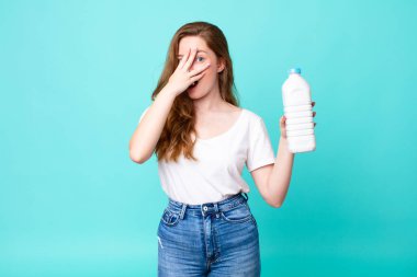 Şok olmuş, korkmuş ya da dehşete düşmüş bir halde. Yüzü elle kaplanmış ve elinde süt şişesi tutuyordu.