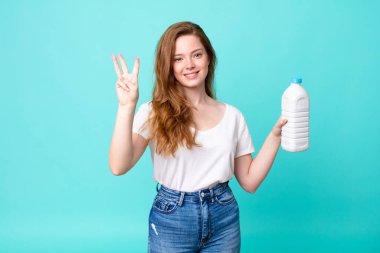 Gülümsüyor ve arkadaş canlısı görünüyor, üç numarayı gösteriyor ve elinde bir süt şişesi var.