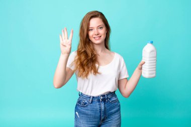 Gülümsüyor ve arkadaş canlısı görünüyor, dört numarayı gösteriyor ve elinde bir süt şişesi var.