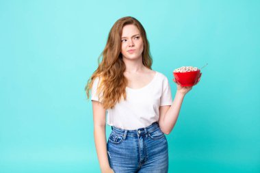 Güzel kızıl saçlı kadın üzgün, üzgün ya da kızgın hissediyor ve elinde bir kahvaltı kasesi tutuyor.