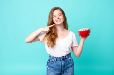 Güzel, kızıl saçlı, kendine güvenen, gülümseyen ve elinde kahvaltı kasesi tutan bir kadın.