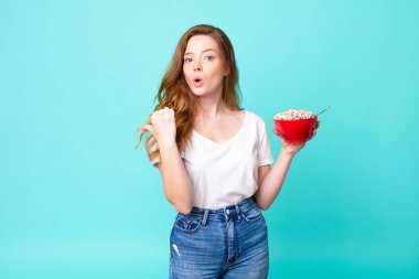 Güzel kızıl saçlı kadın, inanamadığı için şaşırmış görünüyor ve elinde bir kahvaltı kasesi tutuyor.