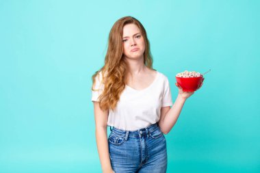 Güzel kızıl saçlı kadın üzgün ve mızmız görünüyor. Mutsuz görünüyor, ağlıyor ve elinde kahvaltı kasesi tutuyor.