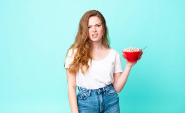 Güzel kızıl saçlı kadın şaşkın ve kafası karışık ve elinde bir kahvaltı kasesi tutuyor.