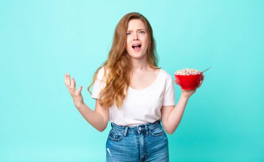 Güzel kızıl saçlı kadın umutsuz, sinirli ve stresli görünüyor ve elinde bir kahvaltı kasesi tutuyor.