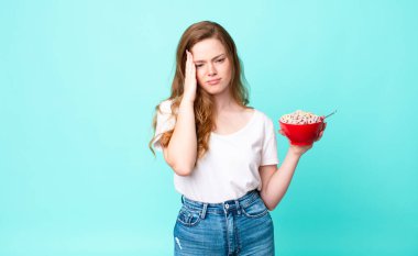 Güzel, kızıl saçlı bir kadın yorgun ve uykulu bir şekilde sıkılmış hissediyor ve elinde kahvaltı kasesi tutuyor.