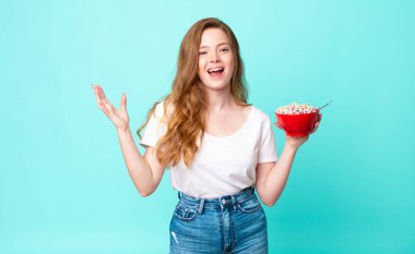 Güzel kızıl saçlı kadın kendini mutlu hissediyor, bir çözüm ya da fikir bulduğunda şaşırıyor ve elinde bir kahvaltı kasesi tutuyor.