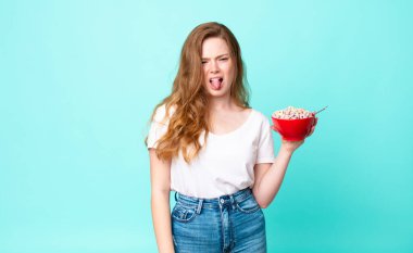 Güzel kızıl saçlı kadın iğreniyor ve sinirleniyor. Dilini dışarı çıkarıyor ve elinde bir kahvaltı kasesi tutuyor.