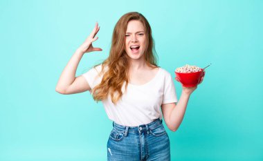 Güzel kızıl saçlı kadın ellerini havaya kaldırıp bağırıyor ve elinde bir kahvaltı kasesi tutuyor.