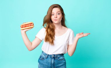 Kızıl saçlı, güzel bir kadın kafası karışık, kuşkulu ve elinde sosisli sandviç tutuyor.