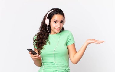 Güzel İspanyol bir kadın kafası karışmış, kafası karışmış ve kulaklık ve akıllı telefonlardan şüphe duyuyor.