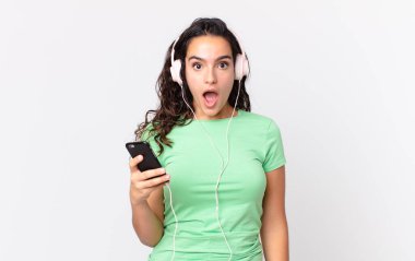Güzel İspanyol bir kadın kulaklıkla ve akıllı telefonuyla şok olmuş ya da şaşırmış görünüyor.