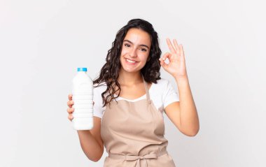 İspanyol güzel aşçı kadın kendini mutlu hissediyor. Onayını gösteriyor. Jest yapıyor ve elinde süt şişesi tutuyor.