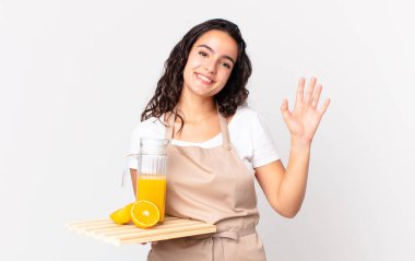 İspanyol güzel aşçı kadın mutlu bir şekilde gülümsüyor, el sallıyor, seni selamlıyor ve portakal suyu tutuyor.