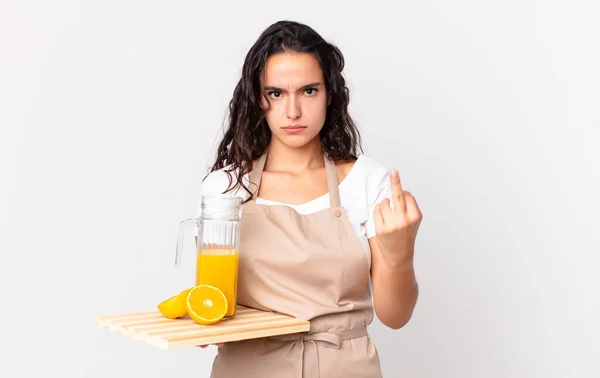 ヒスパニック可愛いシェフの女が怒り いらいらし 反抗的で攻撃的でオレンジジュースを持っていて — ストック写真