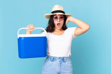 Güzel İspanyol bir kadın stresli, endişeli ya da korkmuş hissediyor. Elleri başının üzerinde taşınabilir bir buzdolabı tutuyor.