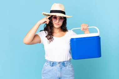 Güzel İspanyol bir kadın kafası karışık ve şaşkın hissediyor. Elinde taşınabilir bir buzdolabı tutarak deli olduğunu gösteriyor.