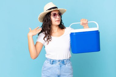 Güzel İspanyol bir kadın stresli, endişeli, yorgun ve hayal kırıklığına uğramış bir şekilde taşınabilir buzdolabını tutuyor.