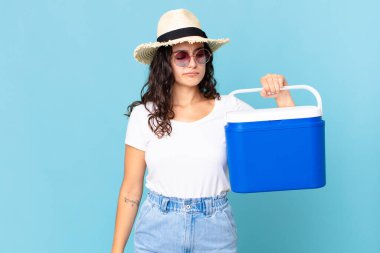 Güzel İspanyol bir kadın üzgün, üzgün ya da kızgın hissediyor ve elinde taşınabilir bir buzdolabı tutuyor.