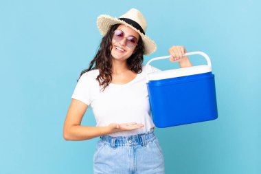 Güzel İspanyol kadın neşeyle gülümsüyor, mutlu hissediyor ve portatif buzdolabı tutan bir konsept gösteriyor.